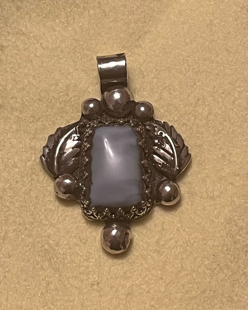 A silver pendant with a blue stone on it.