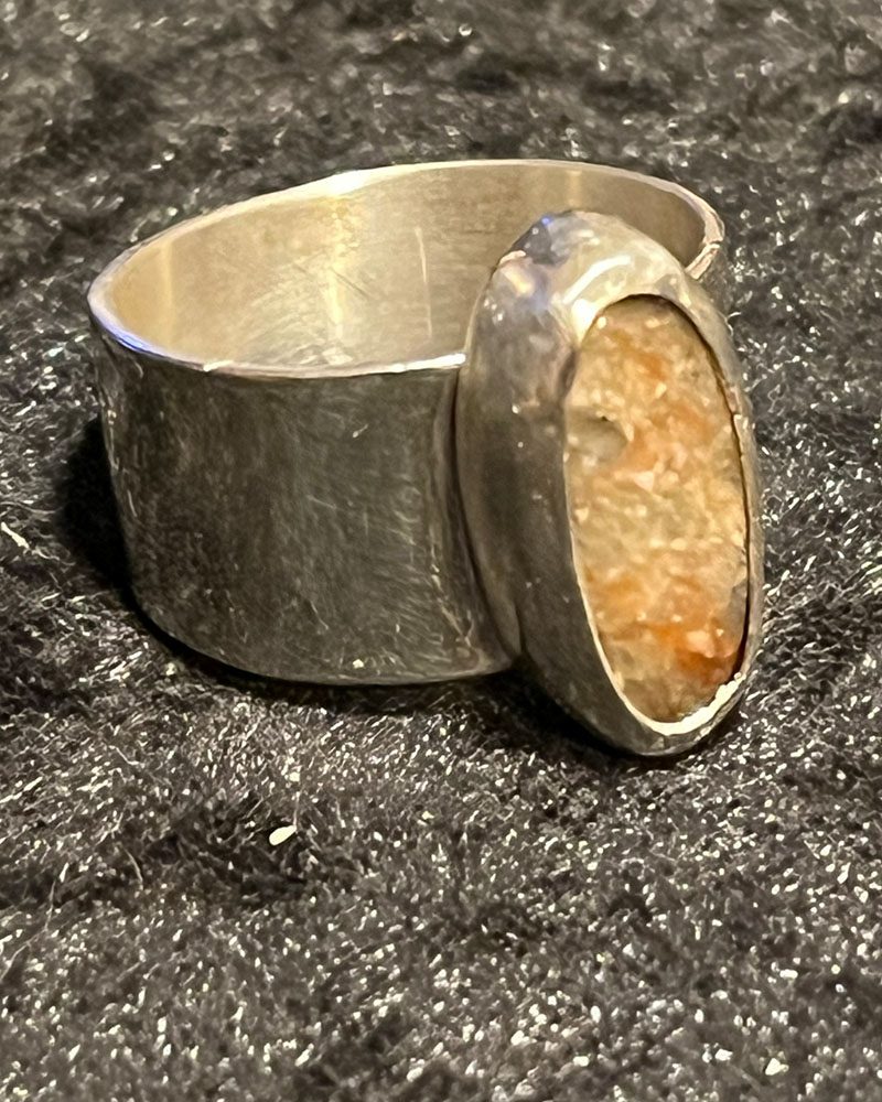 A silver ring with an orange stone on it.
