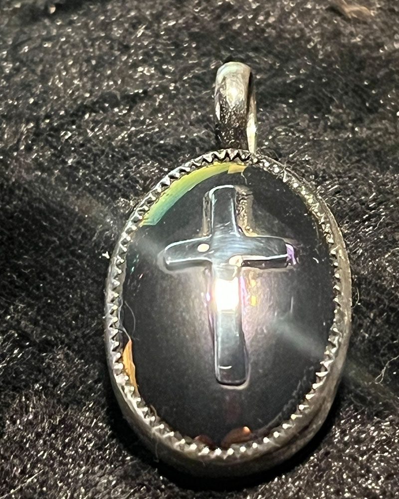 A cross is shown in the middle of a silver oval.