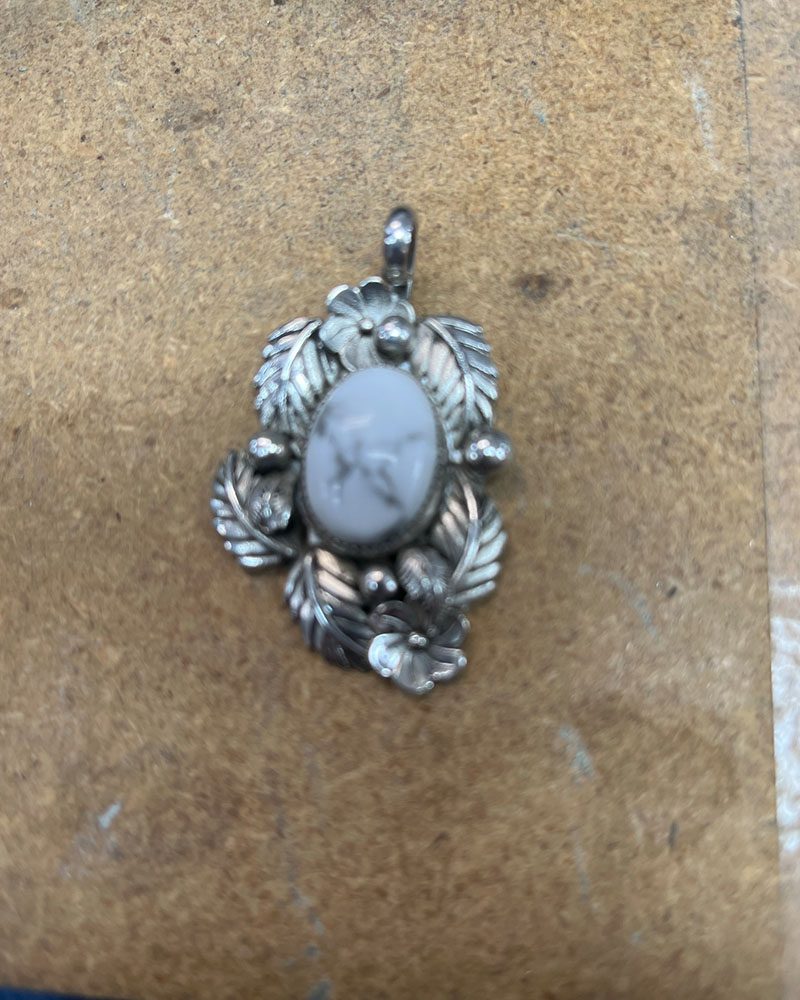 A silver pendant with leaves and a stone.