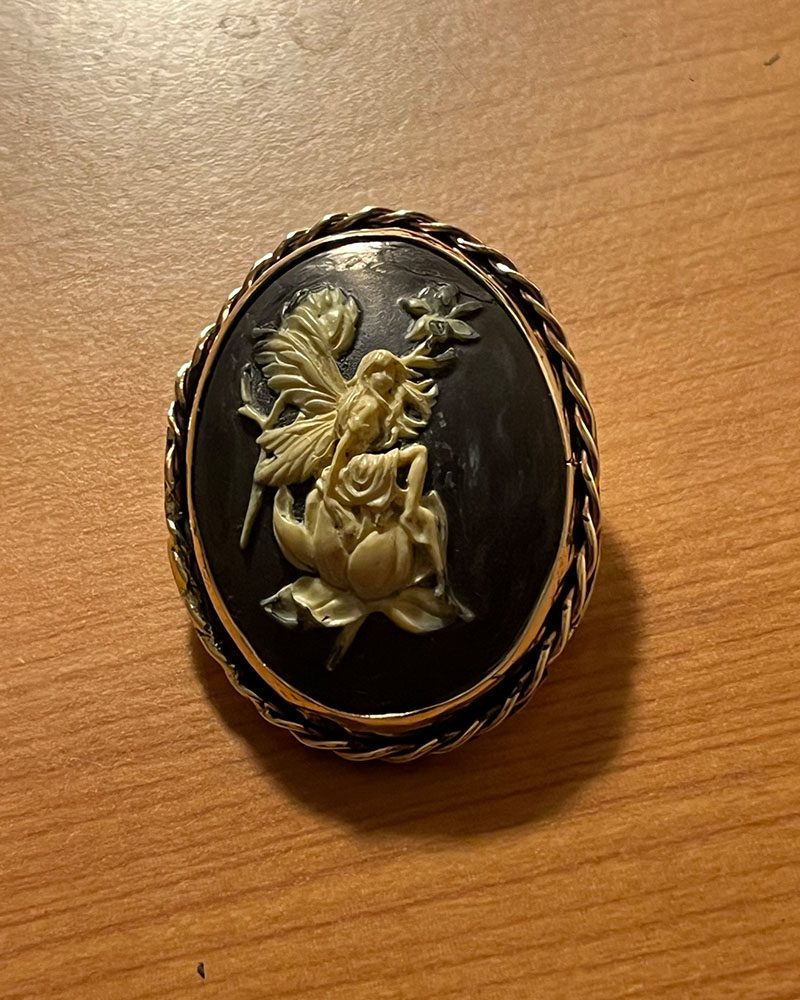 A black and gold brooch with an angel on it.