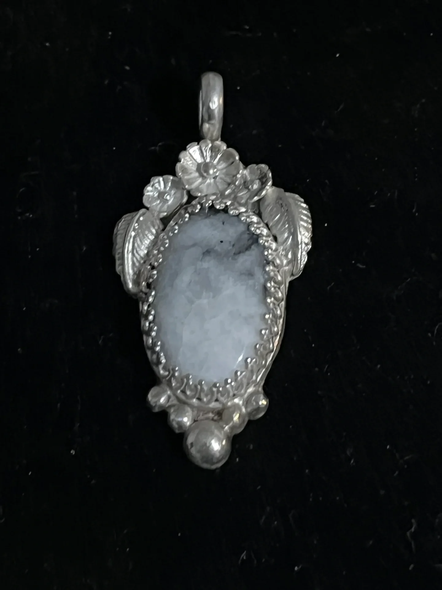 A silver pendant with a blue stone in the middle.