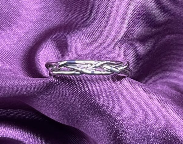 Silver braided ring on purple fabric.