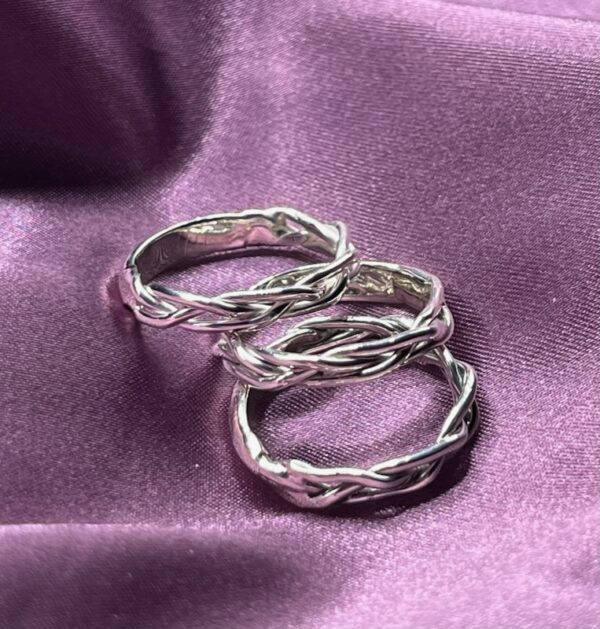 Three silver braided rings on purple fabric.